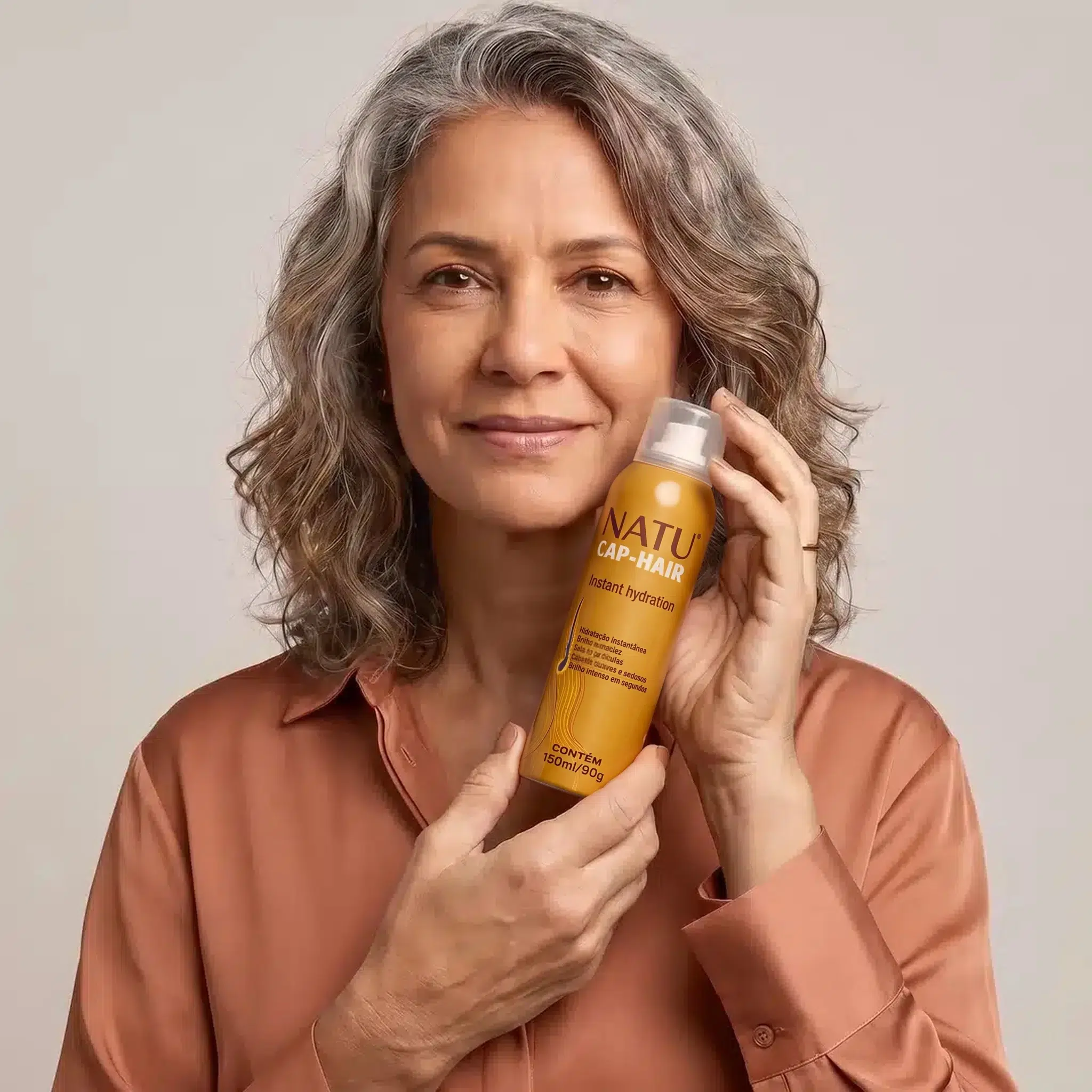 Mulher de cabelo grisalho segurando o spray Hidratação Instantânea Natucap Hair